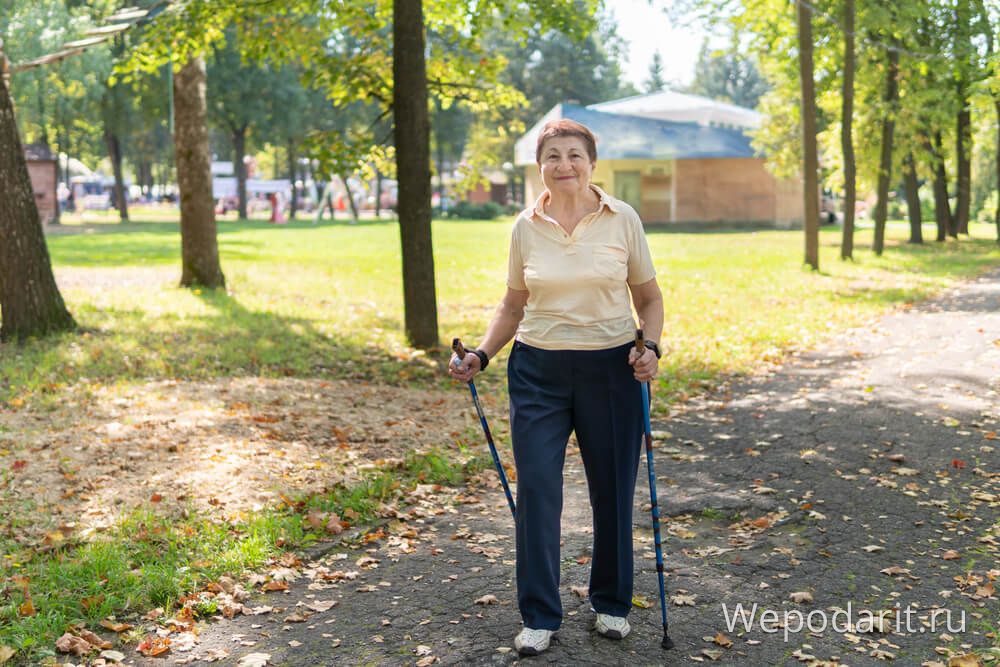 Літня жінка гуляє з палицями по парку